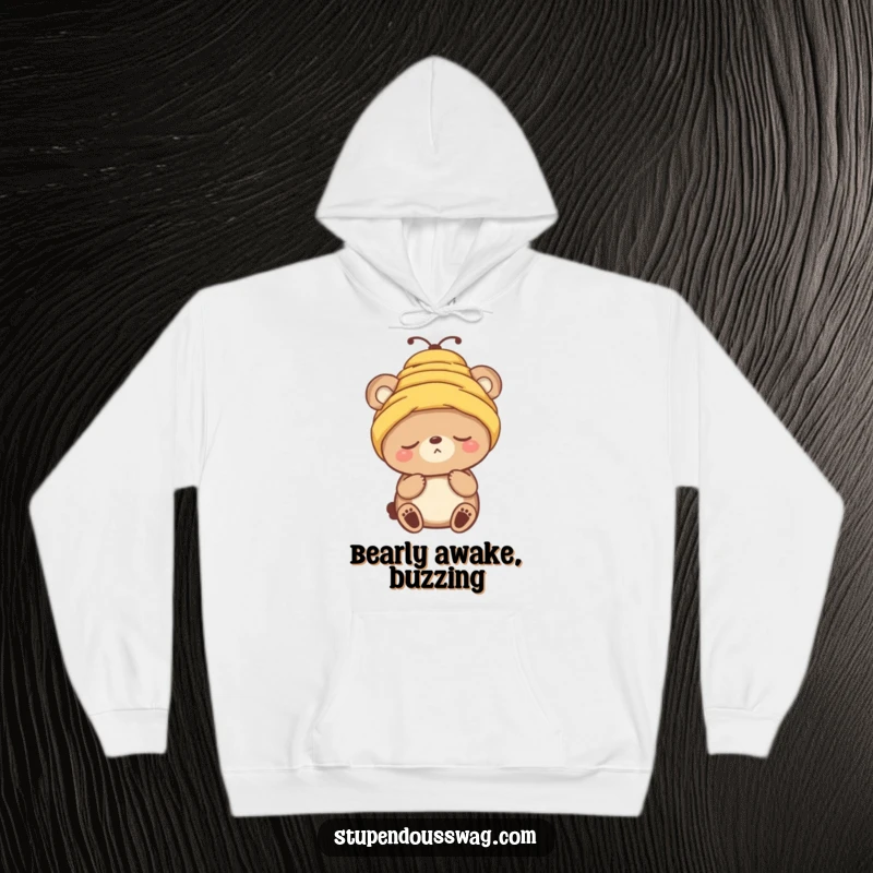 Funny hoodie with a sleepy bear character attempting to wear a beehive as a hat, looking utterly unbothered. Cozy and comical.
